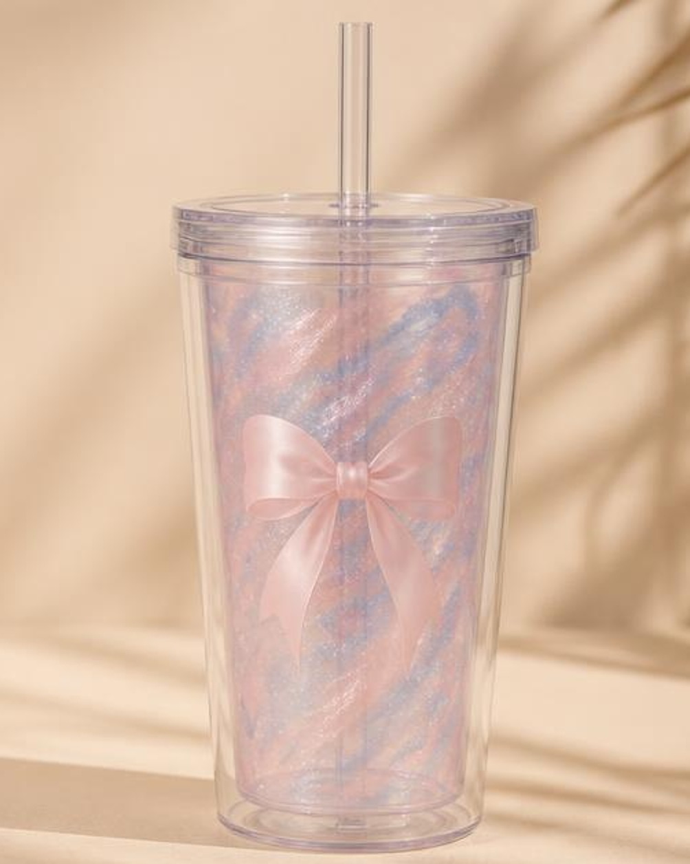 A double-walled reusable tumbler with pink and blue mica swirls and a pink bow decal